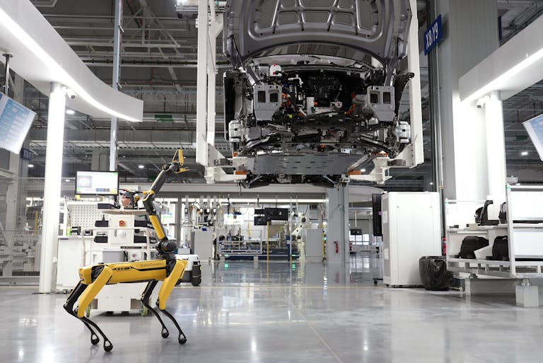 A robotic dog oversees an automated car assembly in a high-tech factory setting.