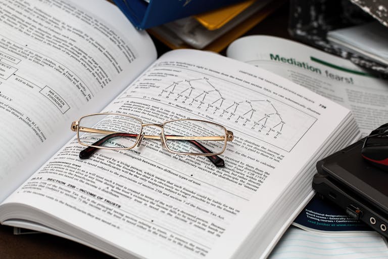 An open book with reading glasses, surrounded by study materials and a laptop, ideal for education themes.